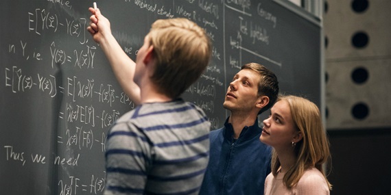 En studerende forklarer matematiske formler på en tavle for to andre studerende