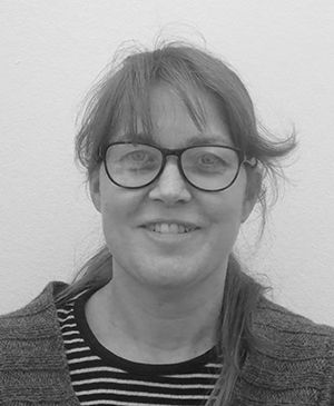 Black-and-white portrait of a woman wearing glasses Black-and-white headshot of a smiling woman with glasses, a striped shirt, and a cardigan against a plain wall.