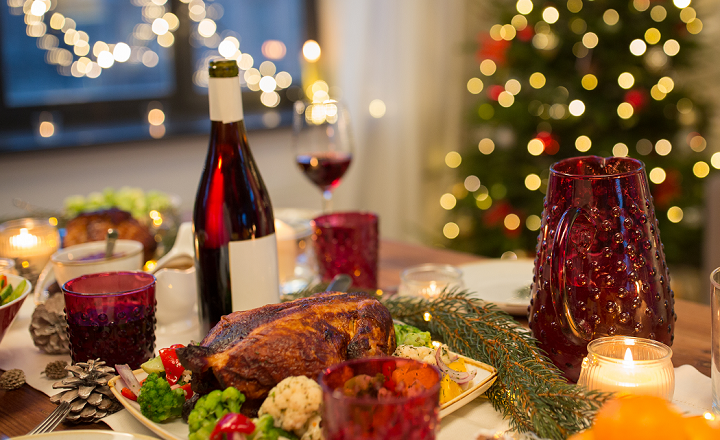 Dækket julebord med stegt kalkun, rødvin, lys og juletræ i baggrunden.