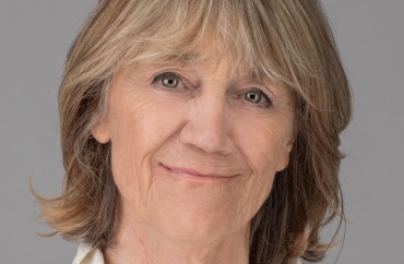 Portræt af smilende kvinde med lyst, skulderlangt hår foran en grå baggrund.