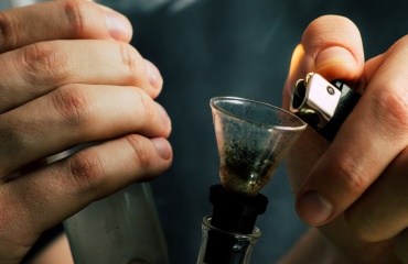 Hænder tænder cannabis i en bong med en lighter.