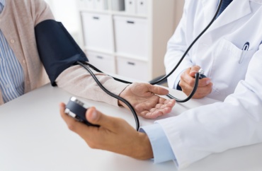 Sundhedsperson måler blodtryk på patient med blodtryksmanchet ved et skrivebord.