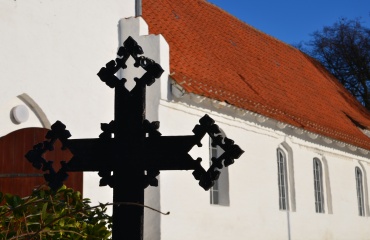 Sort kors i forgrunden foran hvid kirke med rødt tegltag.