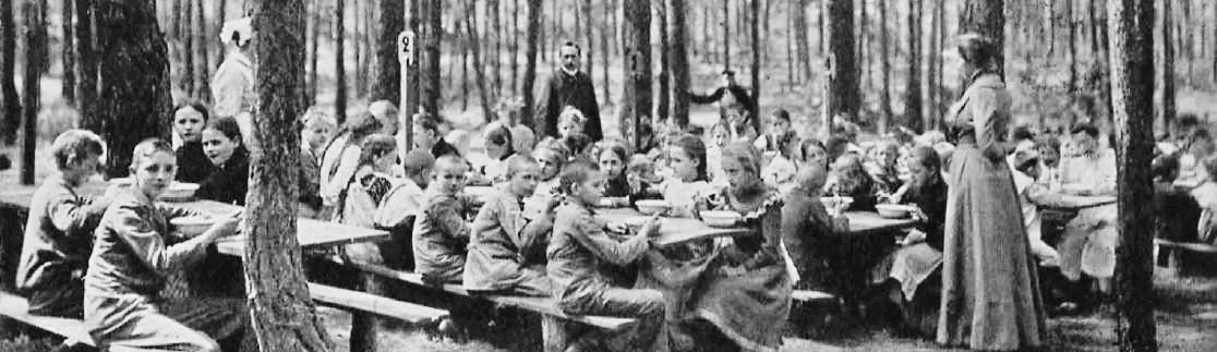 Historisk fotografi af børn i Waldschule Charlottenburg, der spiser frokost i skoven.